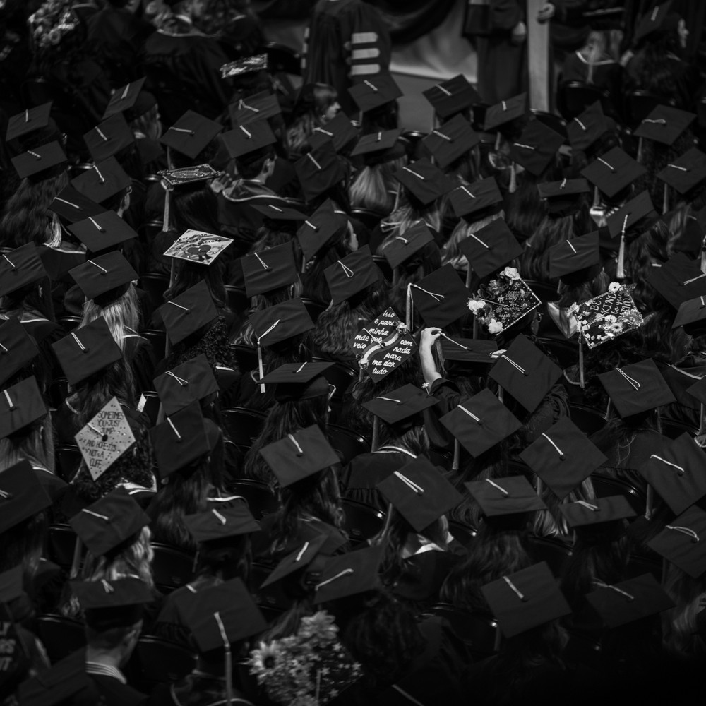 Black and white photograph showing a large group of graduates wearing caps and gowns seated closely together during a graduation ceremony. Photo credit: Michel Thomas, Media Services, UF College of Liberal Arts and Sciences